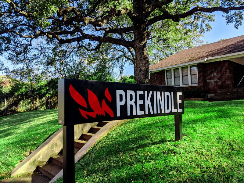 Outdoors photo of Prekindle headquarters, trees, grass, sign with logo